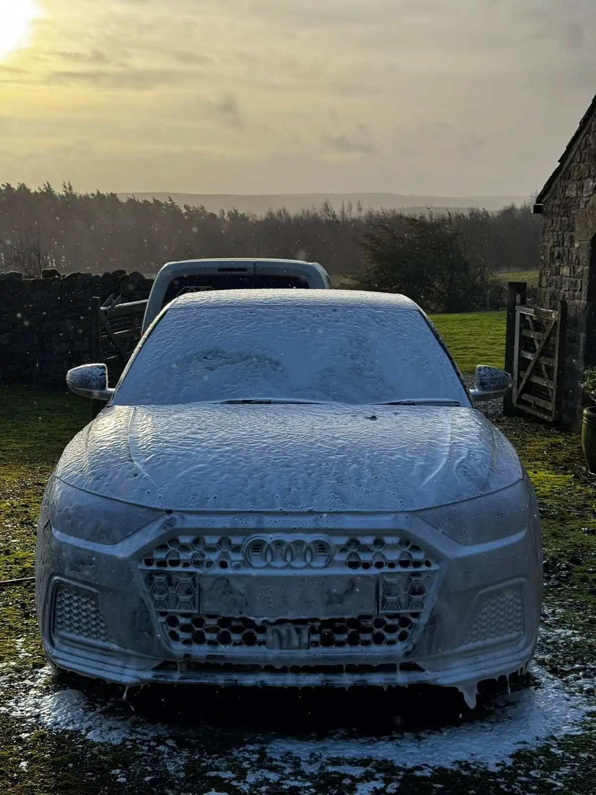 Audi A1 covered in snow foam on a farm driveway at sunrise